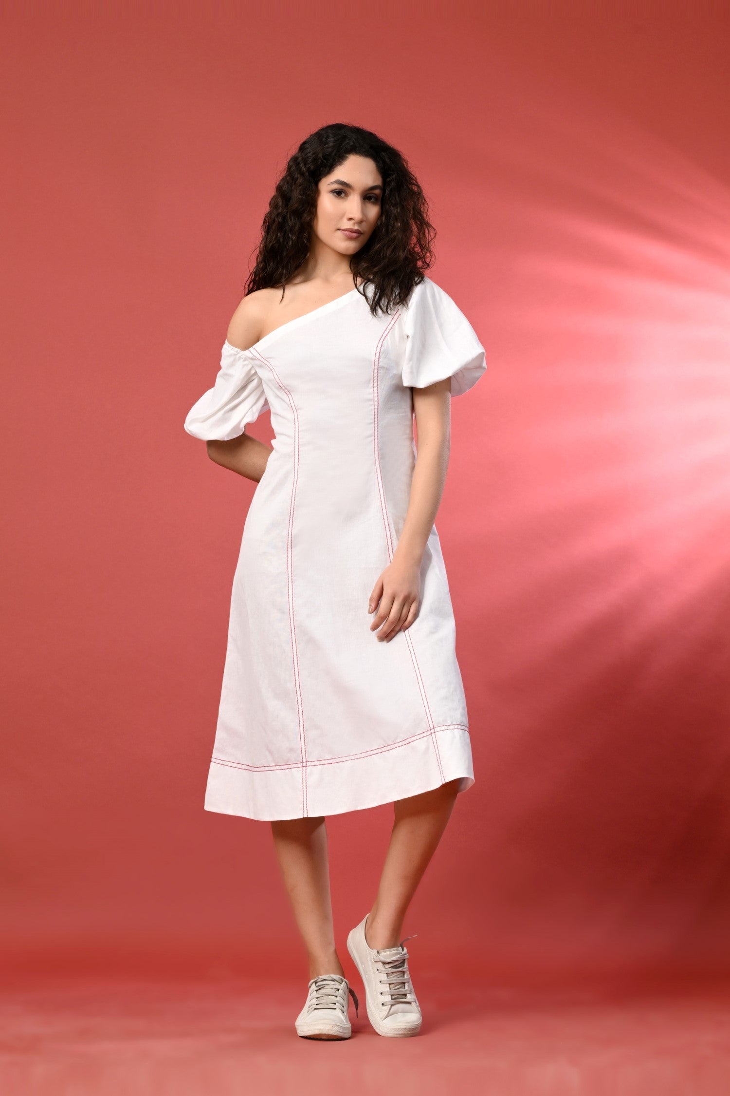 An off-shoulder white linen dress with delicate thread detailing, standing in a sunny, relaxed setting. 