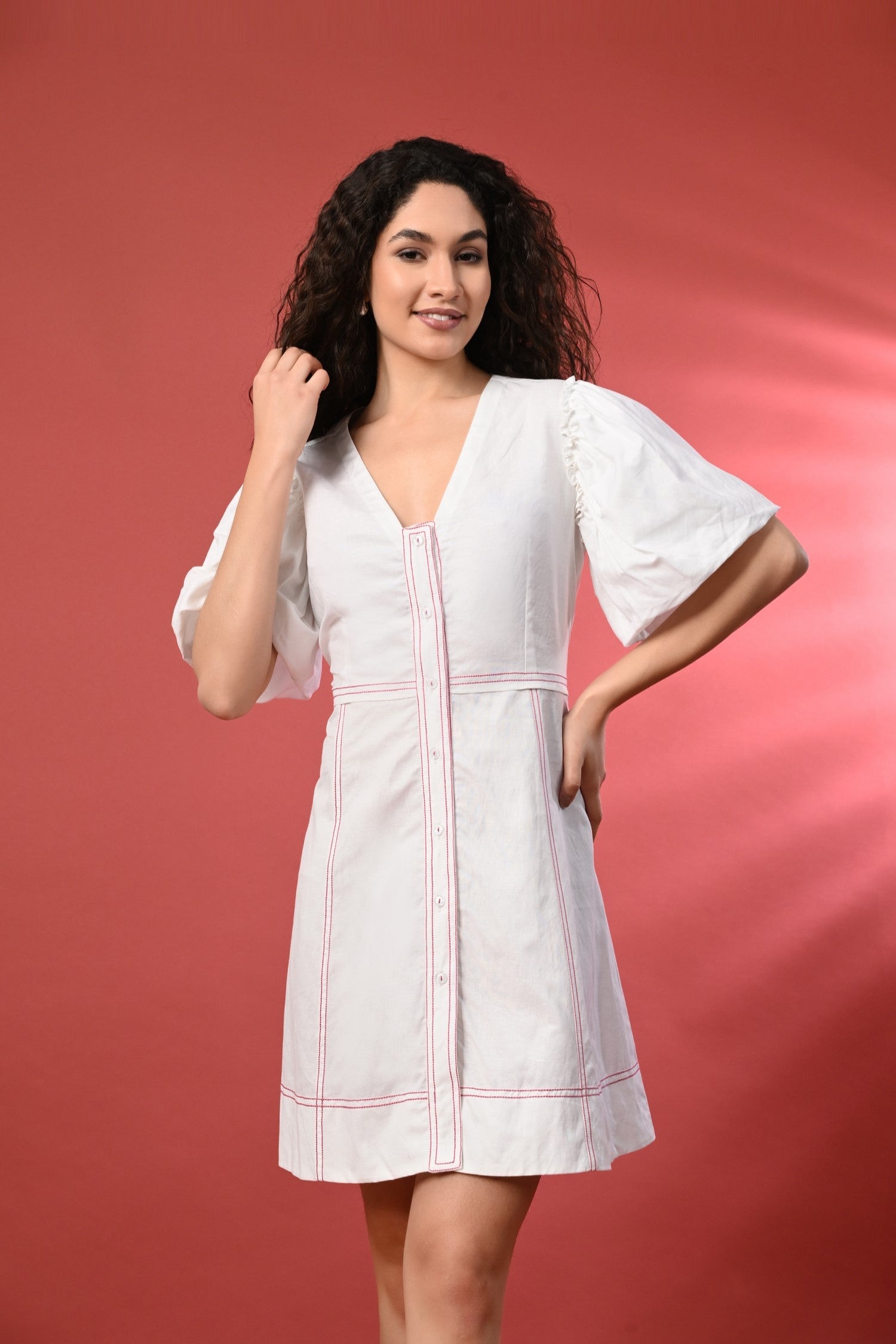 White short cotton dress with delicate thread detailing, standing in a bright summery setting. The dress features a flowy fit