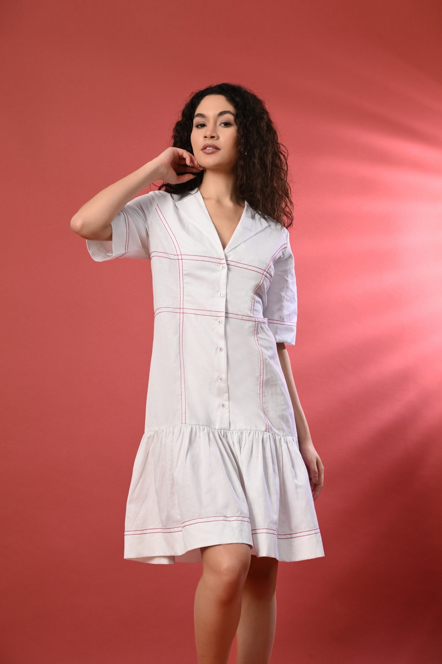 Woman wearing a chic white short sundress with delicate thread detailing, standing in a bright, summery setting. 